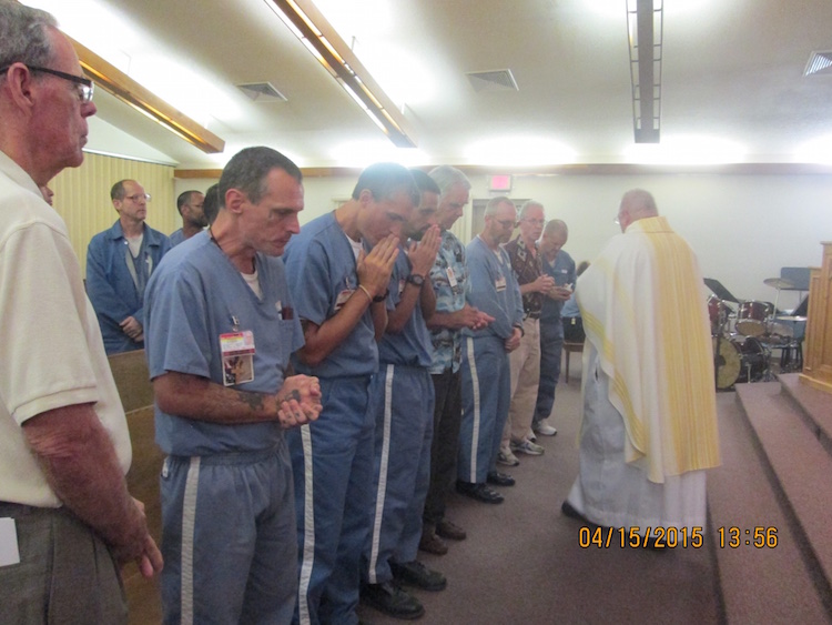 Inmates praying during a chapel service as a minister walks amongst them handing out the eucharist.