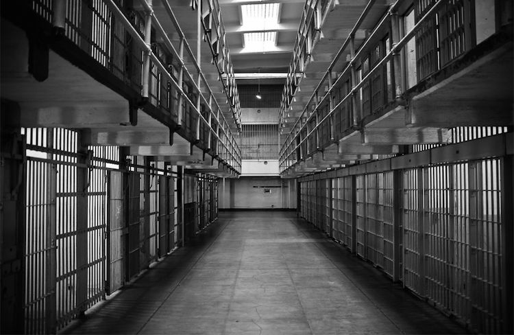 Black and white image of long prison block, empty cells all along the sides.
