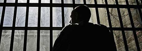 Prisoner looking at a massive razor wire structure through cell bars.